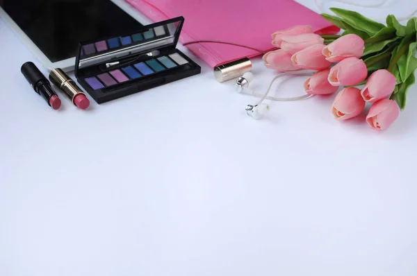 Beauty stuff. Makeup background. Aspects of makeup. Folder, tablet, tulips flowers, headphones, lipsticks and eye shadows on the table.