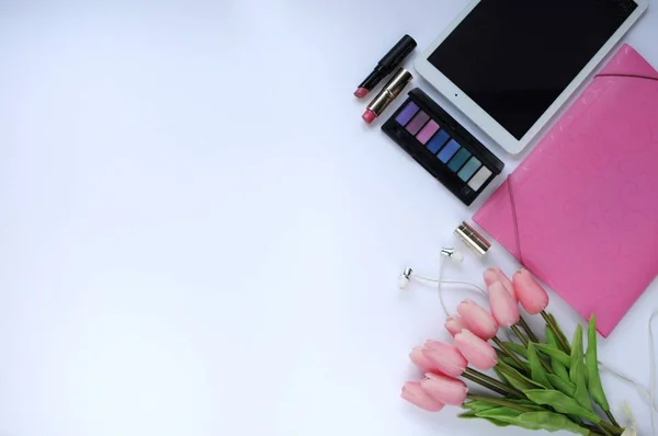 Beauty stuff. Makeup background. Aspects of makeup. Folder, tablet, tulips flowers, headphones, lipsticks and eye shadows on the table.