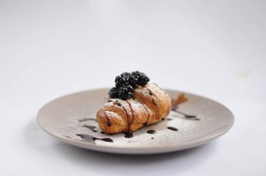 Kruvasan blackberry ile çikolata ve pudra şekeri beyaz arka planda gri plaka üzerinde