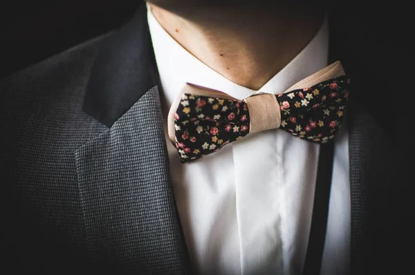 Beautiful brown bow tie with small colorful flowers on white shirt and grey jacket — Stock Photo, Image