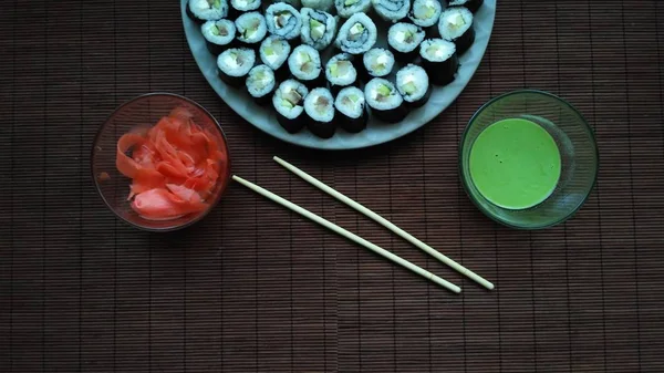 Sushi casero con salsa wasabi, jengibre y palitos de sushi en una alfombra de madera . — Foto de Stock