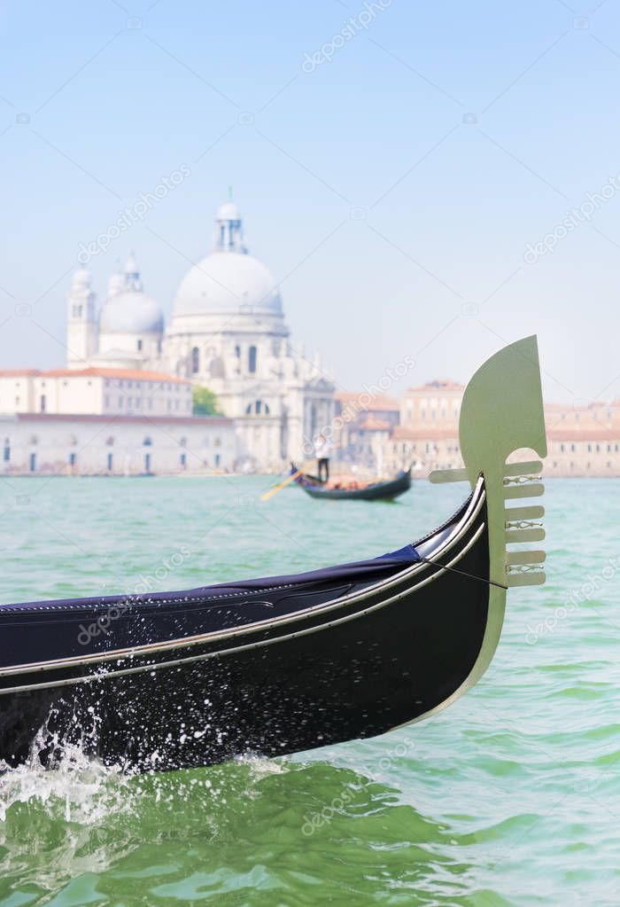 Traditional venetian gondola iron prow-head and gondolier with tourists between Grand Canal and Giudecca Canal of Venice city against basilica Santa Maria della Salute background. Italy.