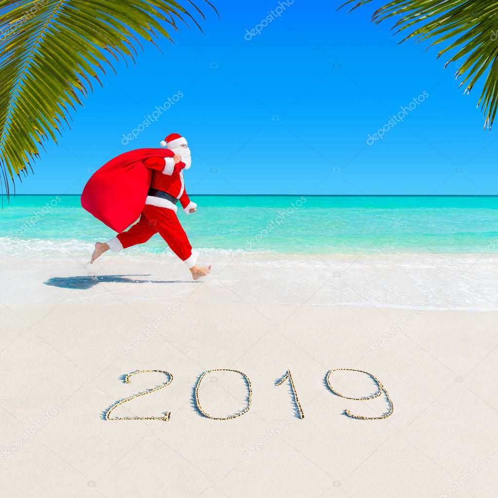 Christmas Santa Claus run at ocean tropical sandy palm beach with large sack full of gifts - season 2019 New Year vacation and travel agencies price discounts concept 