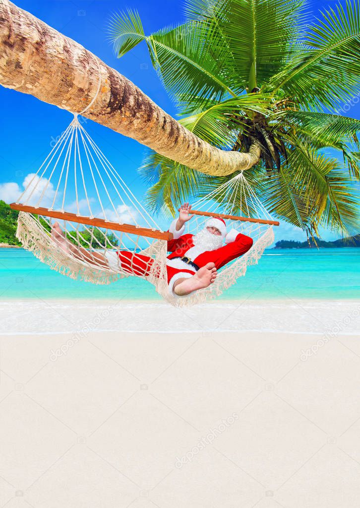 Santa Claus sunbathe in white cozy hammock in shadow of coconut palm tree at sandy ocean island beach. Happy New Year and Merry Christmas travel destinations for tropical vacations,vertical background