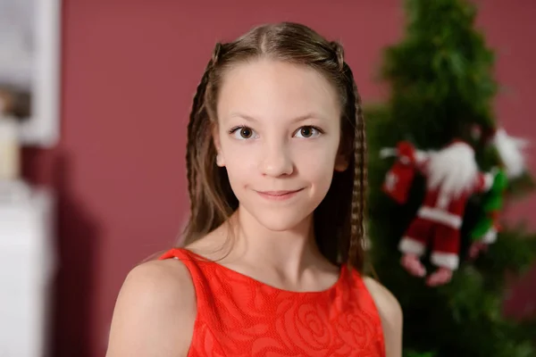 The girl in the red dress next to the white fireplace, decorate a Christmas tree with toys — Stock Photo, Image