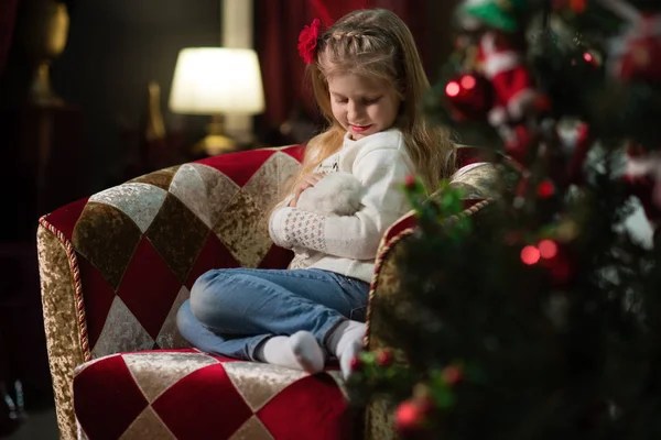 The girl in the red dress next to the white fireplace, decorate a Christmas tree with toys — Stock Photo, Image