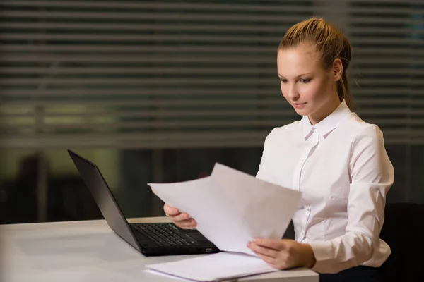 Junge Geschäftsfrau in lässiger Kleidung, am Tisch sitzend, Dokumente genau unter die Lupe nehmend, am Computer arbeitend — Stockfoto