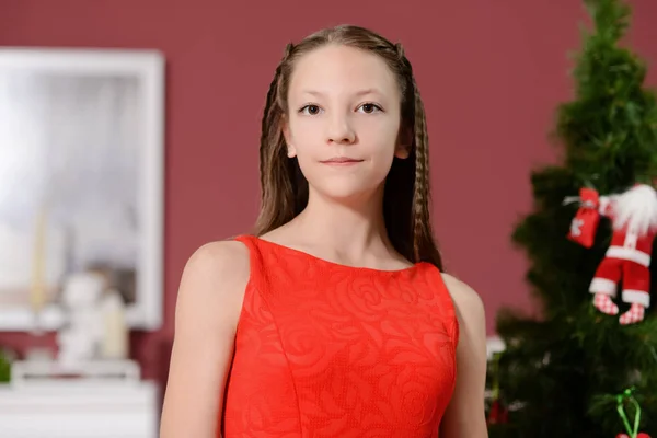 The girl in the red dress next to the white fireplace, decorate a Christmas tree with toys — Stock Photo, Image