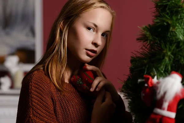The girl in the next to the white fireplace, decorate a Christmas tree with toys — Stock Photo, Image