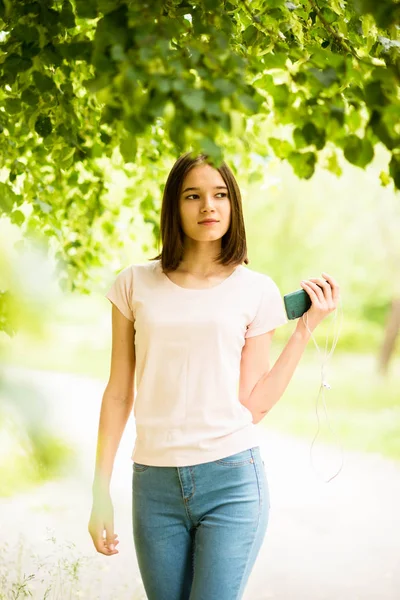 Jovencita morena en camiseta blanca y jeans escuchando música en auriculares — Foto de Stock