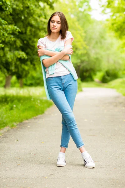 Jovencita morena en camiseta blanca y jeans sosteniendo una chaqueta en sus manos Imágenes De Stock Sin Royalties Gratis