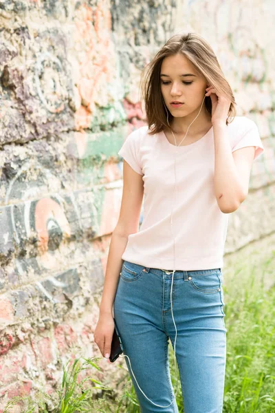 Jovem morena menina em t-shirt branca e jeans ouvir música com fones de ouvido — Fotografia de Stock