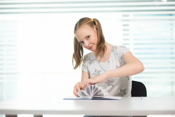 A menina em uma camiseta branca e com caudas sentadas à mesa e brincando — Fotografia de Stock