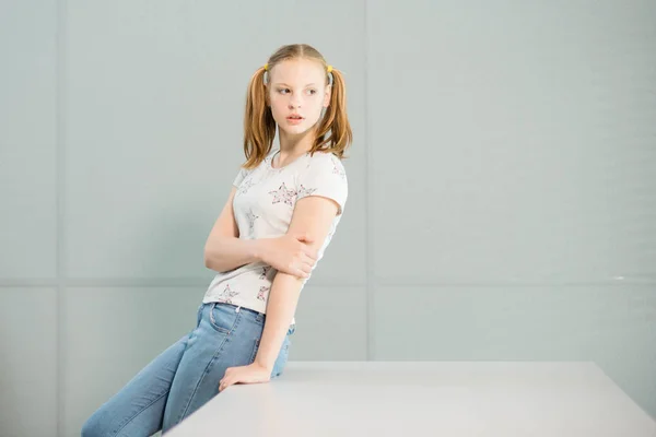 La chica en una camiseta blanca y con colas se para cerca de la mesa — Foto de Stock