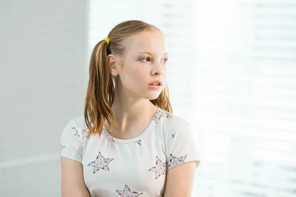 La chica en una camiseta blanca y con colas se para cerca de la ventana — Foto de Stock