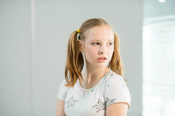 La chica en una camiseta blanca y con colas se para cerca de la ventana — Foto de Stock