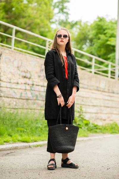 Belle fille aux cheveux longs en lunettes de soleil avec sac en longs vêtements sombres — Photo