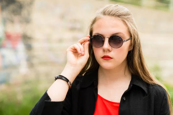 Belle fille aux cheveux longs en lunettes de soleil avec sac en longs vêtements sombres — Photo