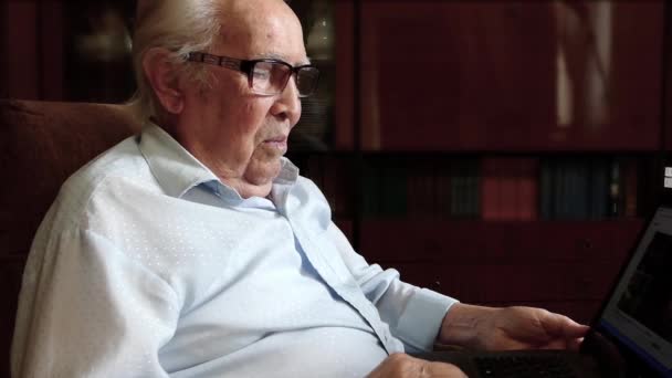 Egy Szemüveges Öregember Egy Karosszékben Könyvtár Hátterében Átnéz Valamit Egy — Stock videók