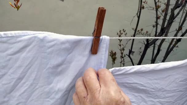 老年人有血肿的老手 手把干净的亚麻布挂在晾衣绳上 并用衣针把它固定住 后续行动 — 图库视频影像