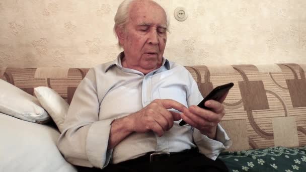 Staruszek Siedzi Pokoju Uśmiecha Się Uczy Pomocą Smartfona Trzymając Rękach — Wideo stockowe