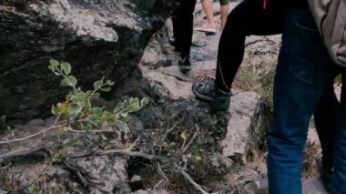 Turistlerin ayakları bir dağ nehrinin kıyısındaki kayalık kayalar boyunca yürür. Turist bacakları bir dağ nehri kıyısındaki kayalık kayalıklara gider..