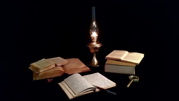 Aufgeschlagene Bücher und ein handgeschriebenes Notizbuch liegen neben einer alten Petroleumlampe. Alte Bücher und eine Petroleumlampe liegen auf schwarzem Hintergrund.