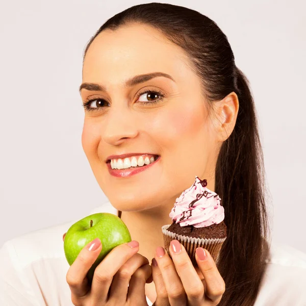 美丽的微笑的女人拿着一个绿色的苹果和一个蛋糕甜点在白色背景 健康饮食和不健康的饮食概念 — 图库照片