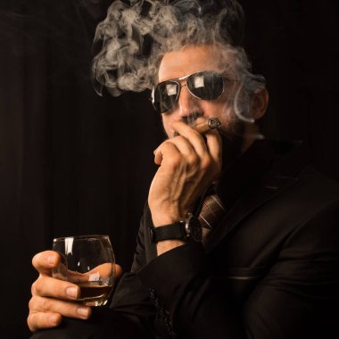 Siyah takım elbise ve güneş gözlüğü beyefendi puro sigara ve alkol siyah arka plan üzerine.