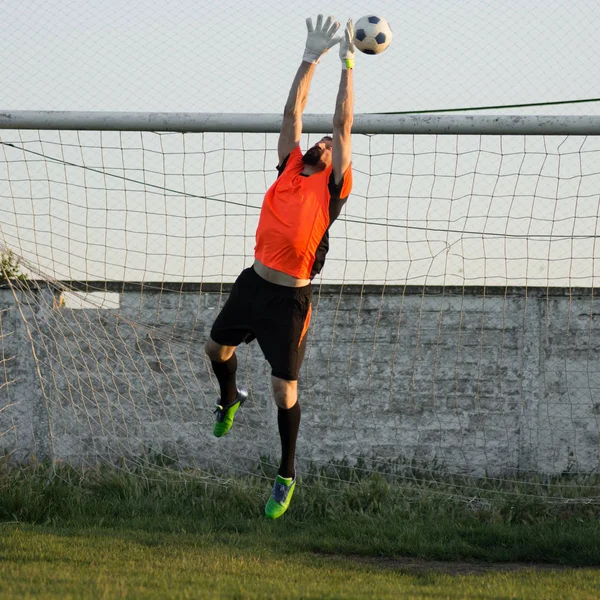 Kaleci futbol topu futbol oynarken yüksek atlıyor.