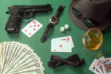 Nesne üzerinden kumar casino, kart, papyon, tabanca, silah, silah, kol saati, şapka, içki, alkol, para, Amerikan doları, güneş gözlüğü yeşil tablo arka plan, casino aksesuarları, kumar ve suç kavramı içinde için aksesuar grubu.