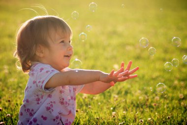 Neşeli şirin bebek kız açık havada yeşil çim zemin üzerine kabarcıkları ile oynuyor.