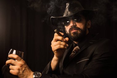 Siyah takım elbise siyah kovboy şapkalı şık beyefendi puro sigara ve alkol siyah arka plan üzerine.