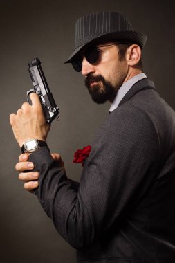 Eski moda şık beyefendi gri arka plan üzerinde elinde bir tabanca tutuyor.
