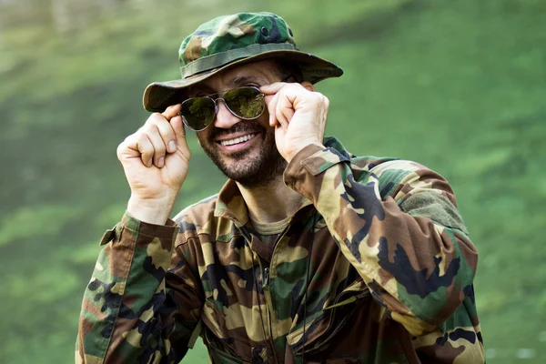 Portrait of smiling park ranger in military uniform and sunglasses on green background.