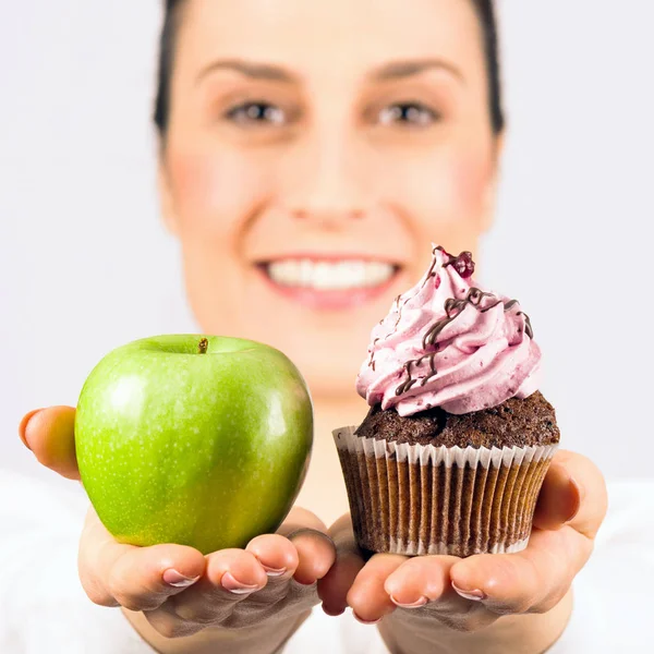 Smiling woman gives a choice, deciding apple or cupcake, healthy or unhealthy food.