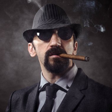 Şapka ve güneş gözlüğü, şık takım elbise eski moda beyefendi dumanlı koyu gri arka plan üzerinde puro portresi.