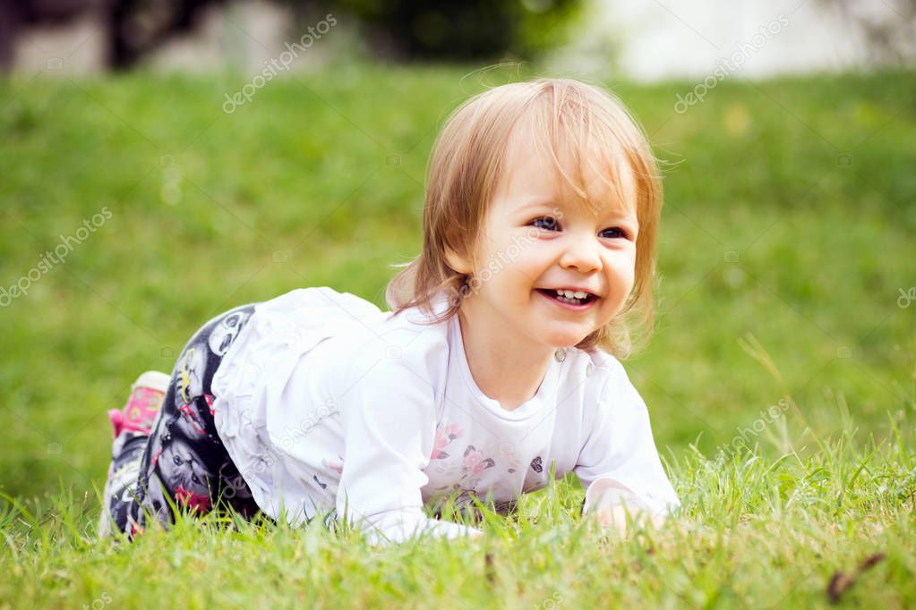 The cute playful smiling baby girl is playing on the grass outdoors.