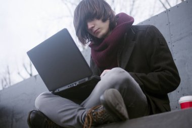 Uzun saçlı trendy genç freelancer adam açık havada laptop kullanıyor.