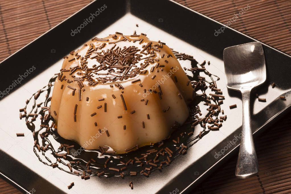 Caramel pudding dessert decorated with sweet sauce and chocolate crumbs on black square plate.