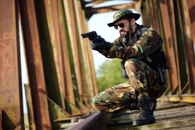 Askeri üniformalı asker demiryolu köprüsüne silah doğrultuyor..