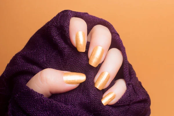 有漂亮的金黄色指甲的女性手 穿着橙色背景的紫色衣服 修指甲概念 — 图库照片#