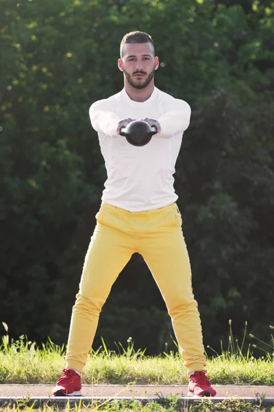 Genç sporcunun ön görüntüsü kettlebell spor ekipmanlarıyla dışarıda egzersiz yapıyor..