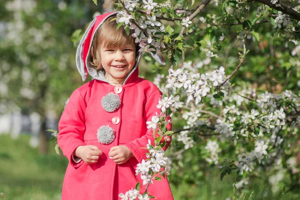 Kırmızı paltolu küçük tatlı kız dışarıda çiçek açan bir dalla duruyor..