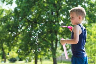 6 yaşındaki tatlı sarı saçlı çocuk sabun köpüğü üflüyor ve onlarla dışarıda oynuyor..