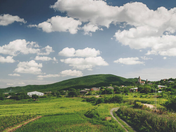 beautiful green fields, hills and cloudy sky near village in georgia
