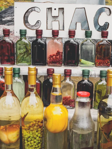 Traditional georgian alcohol drink chacha in bottles with different fruits and herbs at market — Stock Photo