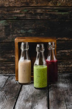 Organic fruit smoothies in glass bottles on wooden background clipart