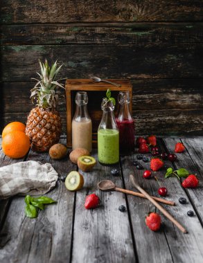 Delicious detox smoothies in glass bottles on rustic wooden board with assorted fruits clipart