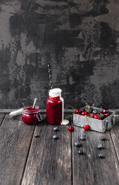 Organic berry smoothie in bottle and jar on wooden background